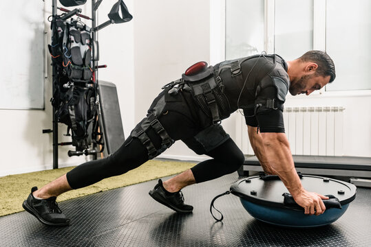 Fitness athlete in electrical muscular stimulation suit doing push-ups on bosu ball