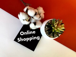 Online shopping on a black sheet of paper .Next to it is cotton and a pot with a flower on a divided orange-white background.