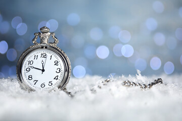 Fototapeta na wymiar Pocket watch on snow against blurred lights, space for text. New Year countdown