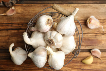 Fresh organic garlic in basket on wooden table, flat lay