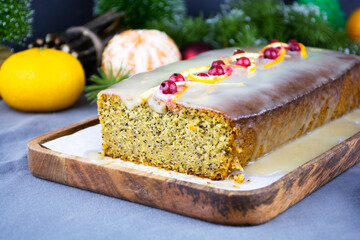 homemade Christmas rectangular sliced lemon cake with glaze and decor on top on a wooden tray on gray table with tangerines, spruce branches