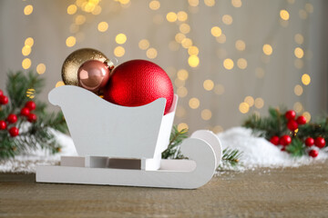 Sleigh with Christmas decorations on wooden table against blurred lights