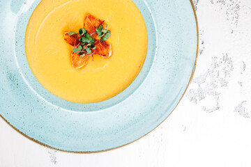 yellow creamy cream soup with salmon in a blue plate on a white background. close up. top view..