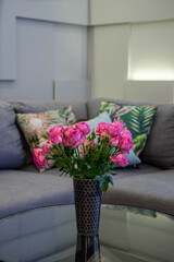 Beautiful bouquet of pink roses in black vase. Cozy couch with cushions. Modern interior. Home decor.