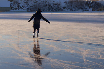 A teenager learns to skate on the ice of a frozen lake in winter.