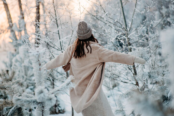 A girl in a beige fur coat is having fun in a fabulous snowy forest. Snowy trees. Fashionable stylish warm winter clothes. 