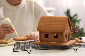 Woman making gingerbread house at white table, closeup