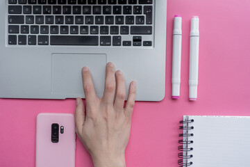High angle shot of a laptop, a cellphone, and writing tools on a pink surface