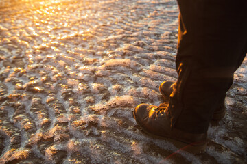 Winter is coming. Female boots on rough slipper ice surface. A woman in brown leather shoes walking on winter sea coastline.