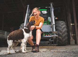 Hof- und Jagdhunde -junge Landwirtin mit ihrem Hund vor einem Traktor, Symbolfoto. © Countrypixel