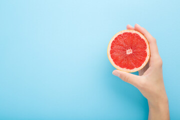 Young adult woman hand holding one half of red grapefruit. Fresh fruit. Empty place for text on light blue table background. Pastel color. Closeup. Top down view.