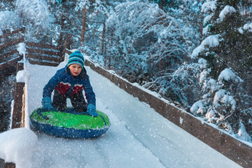 happy kid sliding on tube down snow slide in winter nature