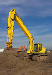yellow used crawler excavator working on a construction site on a sunny day against a blue sky background