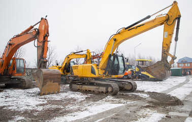 several orange and yellow crawler excavators standing on a construction site. Rent, leasing for earthworks. Snowing, winter.
