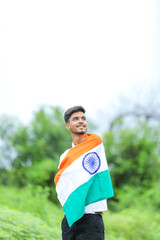 Young indian man waving indian national flag over nature background