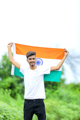Young indian man waving indian national flag over nature background