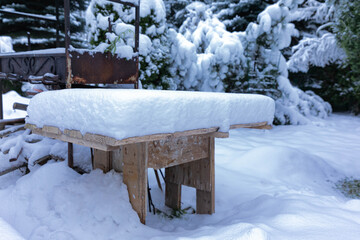snow covered bench.Wooden table covered with a large layer of snow in the garden on the background of the barbecue
