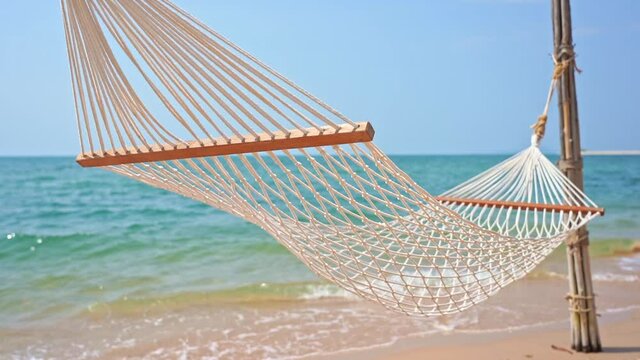 Empty hammock, Rope hammock swinging in the gentle summer breeze blowing along the sandy coast. Breathtaking view of the turquoise ocean waves behind the empty hammock on a tropical island