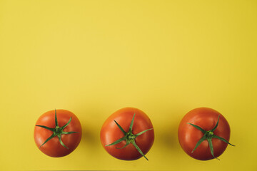 Three red tomatoes on yellow background. Complimentary color style.