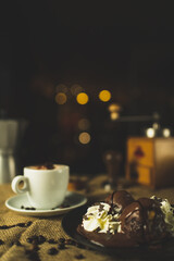 A cup of coffee and a desert, capuccino. A nice composition with a coffee grinder, an espresso maker and some chocolate. Restaurant and coffee shop. Nice creamy bokeh.