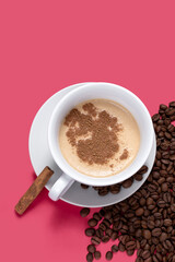 CUP WITH COFFEE WITH MILK AND SOME COFFEE BEANS ISOLATED PINK BACKGROUND