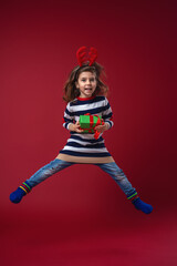 happy smiling girl with gift box in hands and red horns deer on his head, jumps