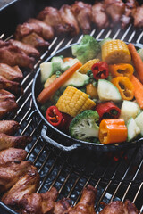 Assorted vegetables and chicken wings on a charcoal grill. Cooking process