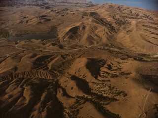 Aerial drone panorama shot of high mountain area, windmills, the long and winding road through the mountains. Southern region, sands, desert, birds eye view, sea shore on the background