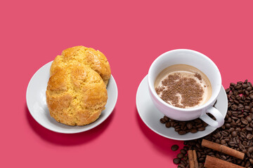 TWO COOKIES ON A WHITE PLATE AND A CUP OF COFFEE WITH MILK AND SOME COFFEE BEANS ON A PINK BACKGROUND