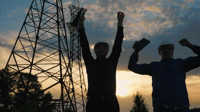 Teamwork. Two engineers at sunset use teamwork software. Success in the work of energy industry engineers. Modern technologies in the energy and telecommunications industry. Power engineers