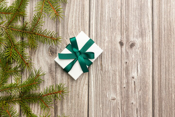 On a wooden background there are branches of a fir tree and gift box with green bow .