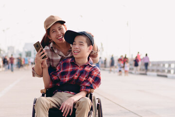 Asian Disabled child on wheelchair and mother in the outdoors nature fun with selfie by smart phone,Life in the education age of special children,Happy disability kid travel in family holiday concept.
