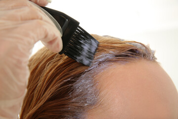 Fototapeta premium Young woman applying dye on hairs indoors, closeup