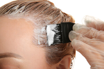 Young woman applying dye on hairs against white background, closeup