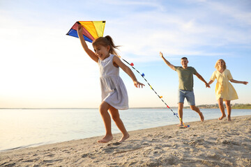 Happy parents with their child playing with kite on beach. Spending time in nature