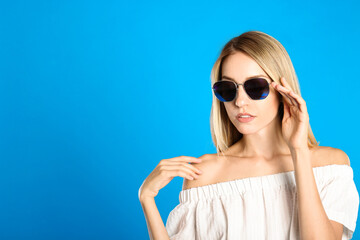 Naklejka premium Beautiful woman in stylish sunglasses on light blue background, space for text