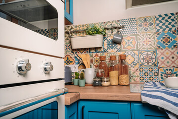 View from the white oven to the modern cozy kitchen with colorful ceramic tiles and a lot of accessories and glass jars with cereals