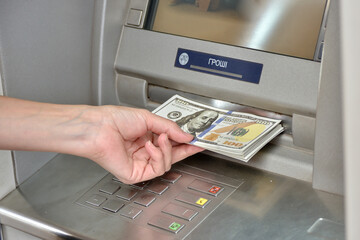 The girl's hand holds a bundle of dollar bills near the ATM.