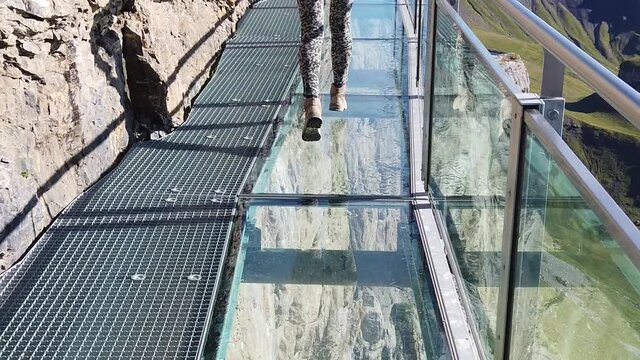 Thrill walk on Schilthorn, Bernese Prealps, Canton of Bern in Switzerland. Caucasian tourist woman walks on a net between high rock faces at mid-station Birg 2677, above village of Murren. SLOW MOTION