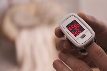 Man measuring oxygen level with modern fingertip pulse oximeter indoors, closeup. Space for text