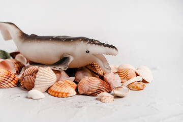 A toy whale is lying on a hill of shells on a white background. Concept of protection of animals