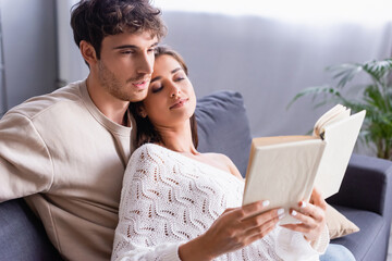 Young woman reading book near boyfriend at home