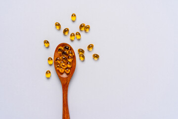 Yellow capsules of vitamin D or fish oil on a wooden spoon
