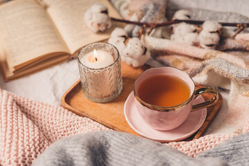 Details of still life in the home interior of living room. Sweater, cup of tea, cotton, cozy, book, candle. Moody. Cosy autumn winter concept. Decoration, vintage with glow bokeh.