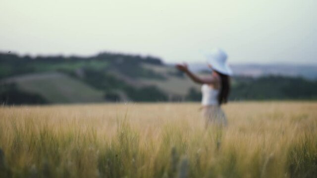 Pretty young woman standing in wheat field opening arms during sunset in summer. Cinematic natural summertime background of girl with warm atmosphere. Natural sunlight and Mediterranean landscape. 4K.