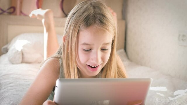 Teenage girl in bed playing a tablet in social internet. Girl watching funny video on the digital tablet.