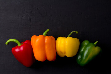 Bright multi-colored bell peppers lie on a black modern concrete background. Red peppers, orange, yellow and green bell peppers. Flat lay, top view, mock up. Copy space