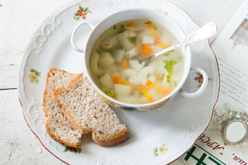 Soup with pasta and white bread on a white wooden background