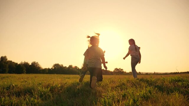 A happy family of children have fun in the park at sunset. Silhouette of fleeing children. Children flee the green lawn in droves. Kids in the park play fun, laugh. Teamwork, playing girls and a boy.