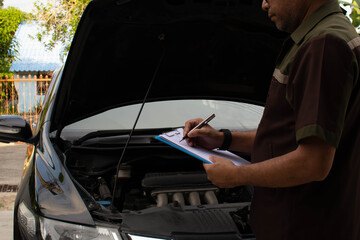 Close-up, A man with a pen is checking a list of auto repair parts to fix the cars. Black cars have...